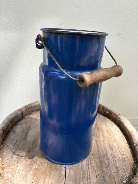 Blaue Emaille-Milchkanne ohne Deckel auf einem Holzfass, Bügel mit Holzgriff