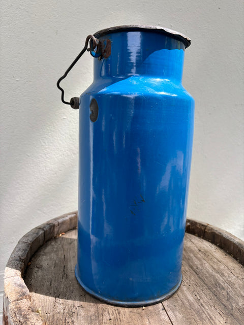Blaue Emaille-Milchkanne mit Bügelgriff, stehend auf einem alten Holzfass