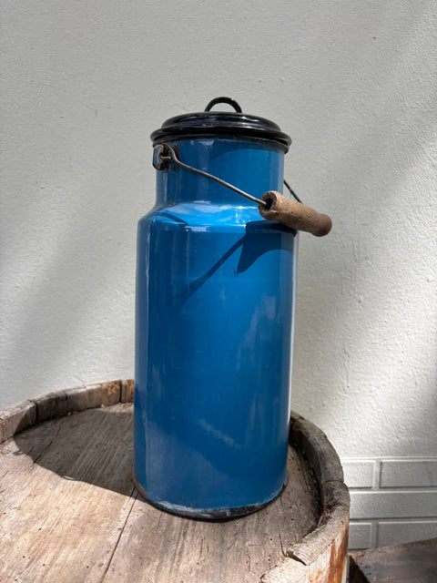 Blaue Emaille-Milchkanne mit Deckel, stehend auf einem alten Holzfass