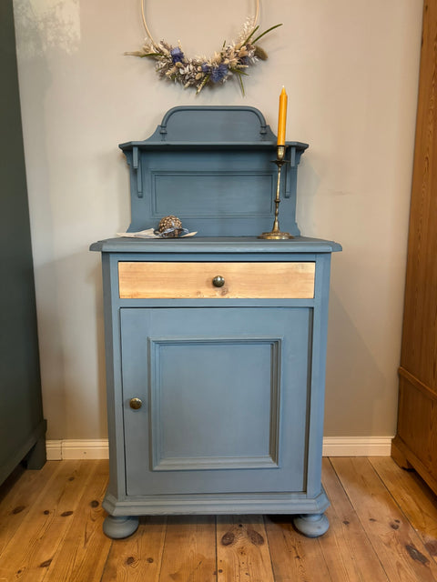 Kleiner alter Nachttisch mit verzierter Holzblende in blaugrauer Kreidefarbe.
