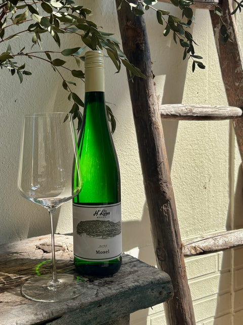 Hermann Ludes Mosel Riesling 2024 Weißweinflasche auf einem Weinglas, hellgelbe Farbe, elegant und frisch wirkend.