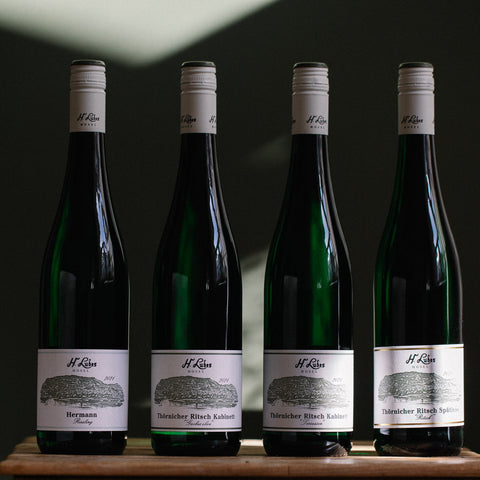 Hermann Ludes Mosel Riesling 2024 Weißwein in einem Weinbrandglas mit goldener Weinfarbe, auf einem Holztisch serviert